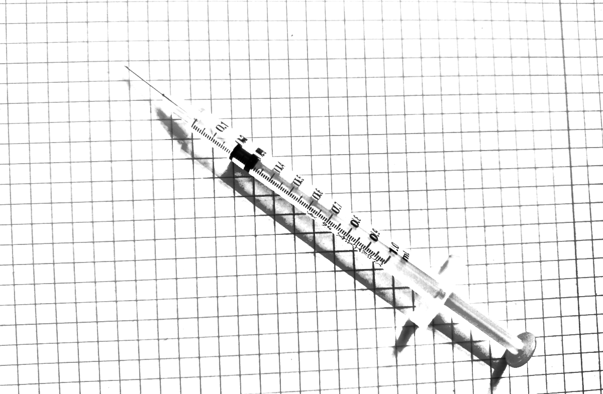 Black and white picture of a syringe resting on a sheet of graph paper.