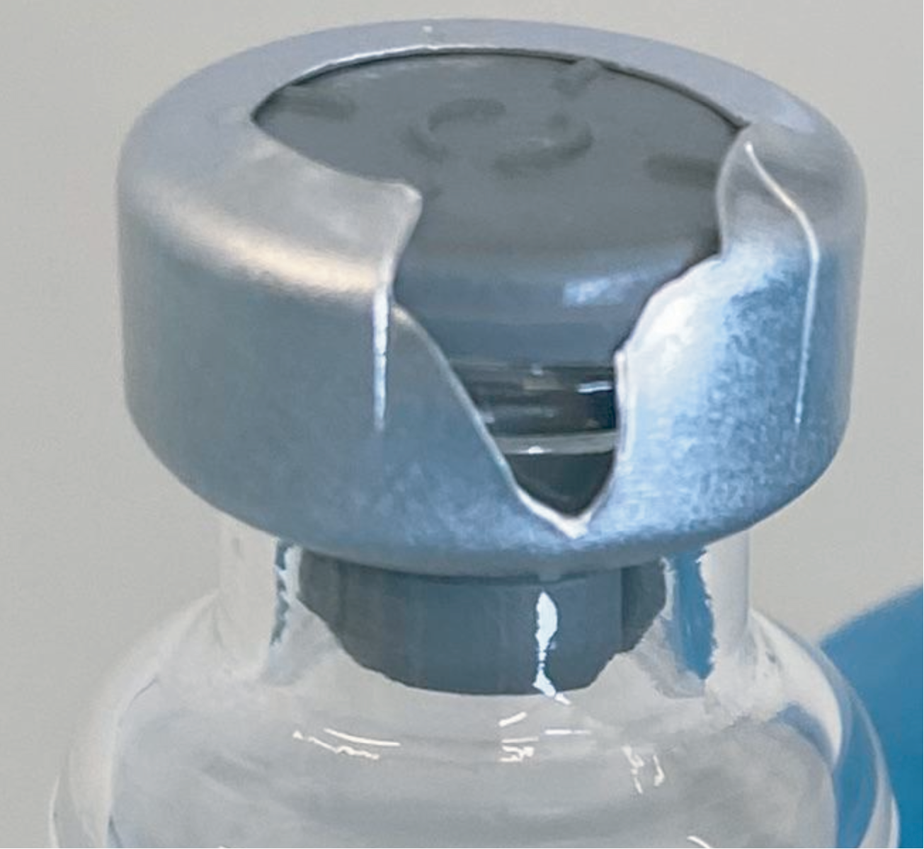 Picture of vial with the metal stopper peeled and ripped all the way to its side, exposing the side of the rubber stopper underneath, with a large red X mark superimposed in the corner.